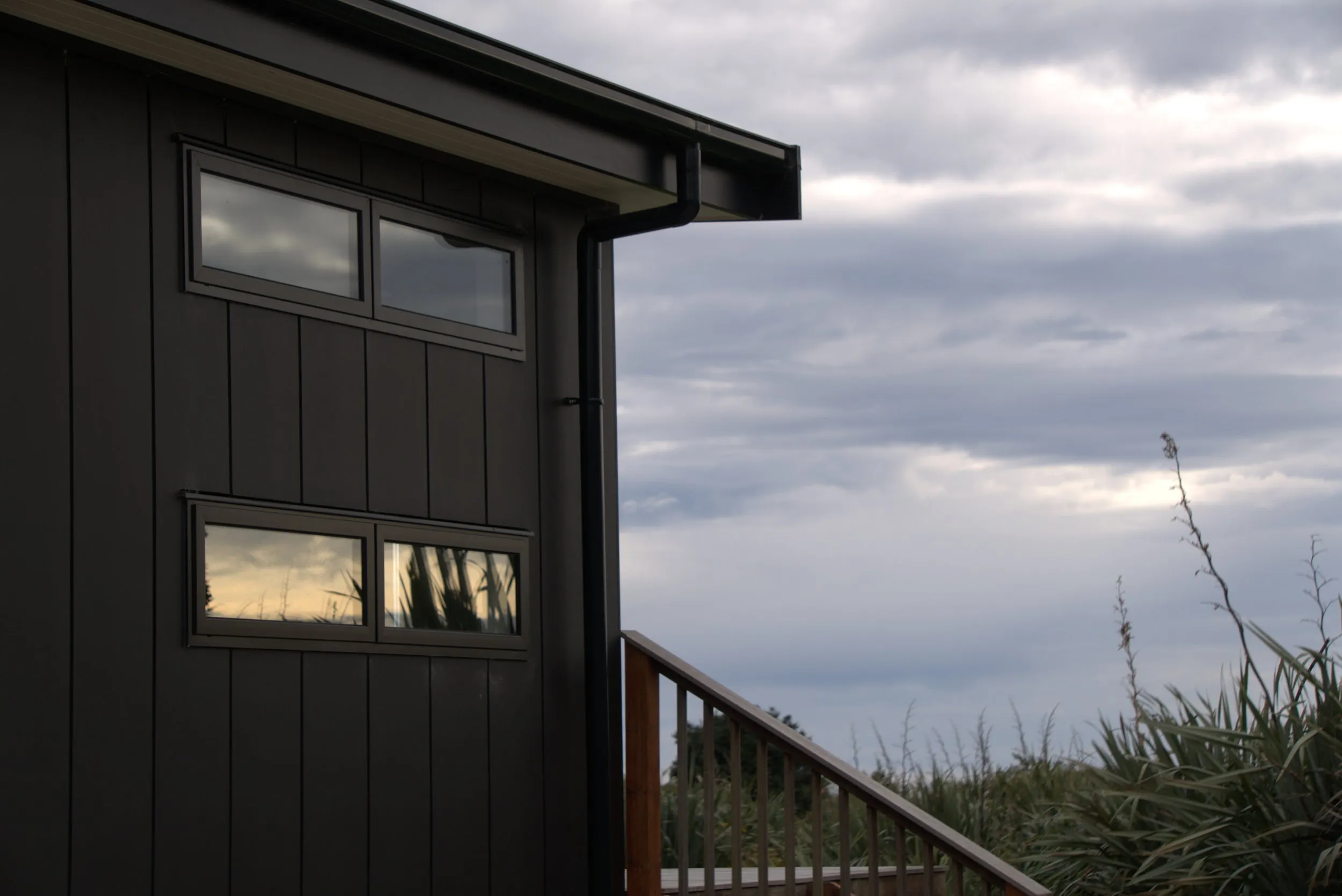 Corner detail of the dark vertical cladding, high ribbon windows and the deck balustrade against an overcast sky