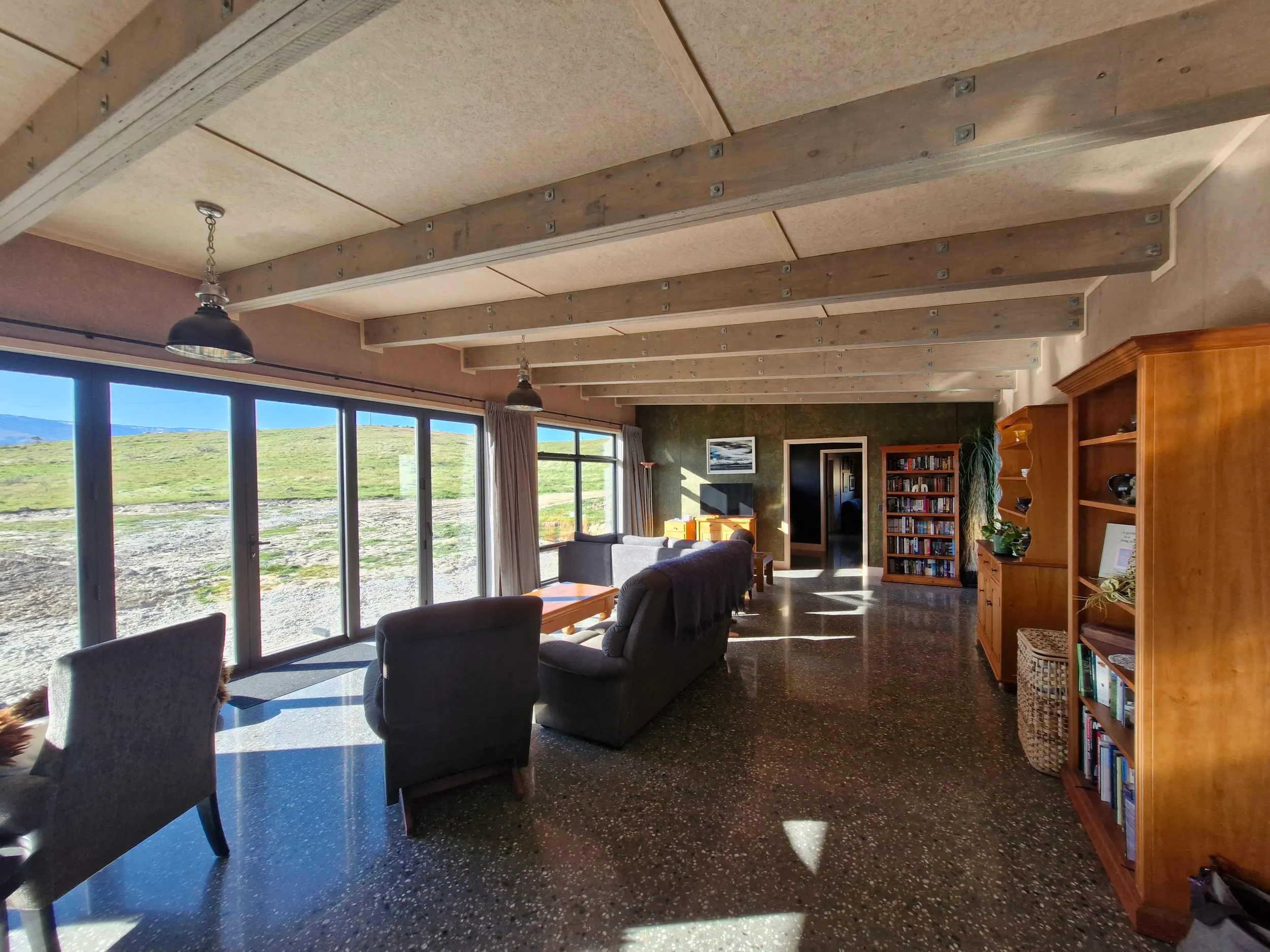 The living space — exposed rafters against a panel-lined ceiling, polished concrete floor, and glazing running the length of the north wall