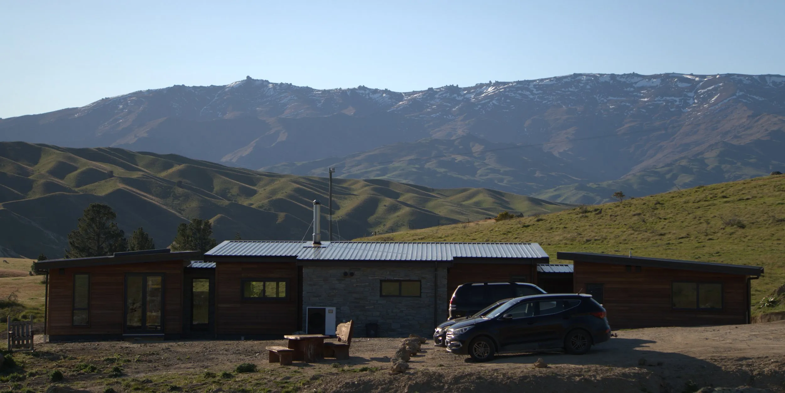 The long elevation in cedar and schist under a standing-seam roof, with the snow-covered Dunstan range behind